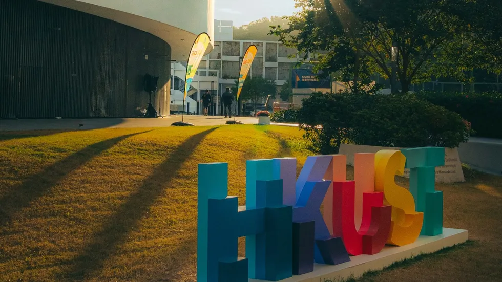 港科大草坪上的彩色 HKUST 字样标识，夕阳光线。