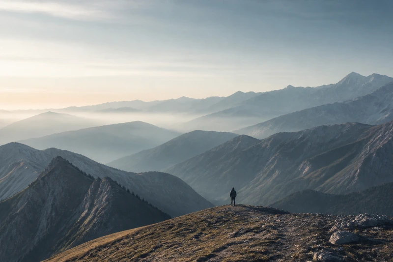 A traveller standing on a ridge and looking across a range of mountains.